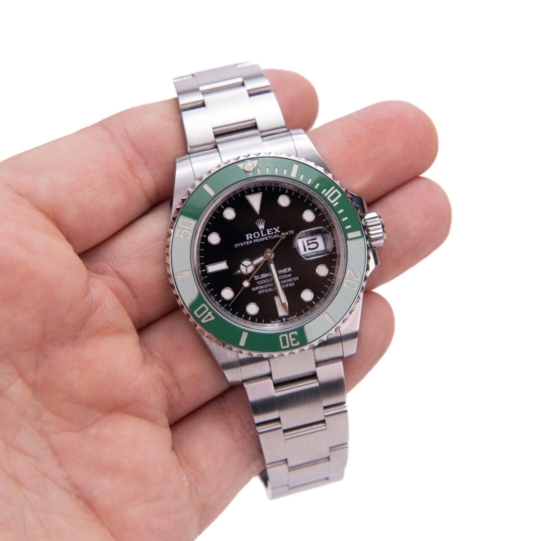 Hand holding a silver watch with green bezel.