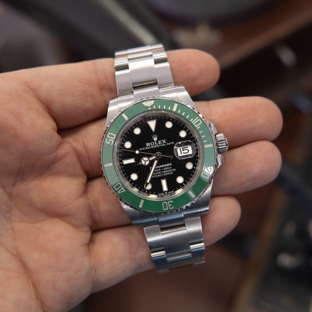 Hand holding silver and green wristwatch.