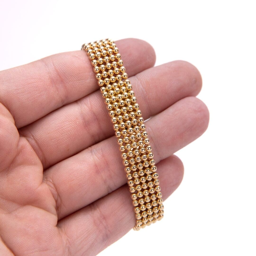 Hand holding a gold beaded bracelet.