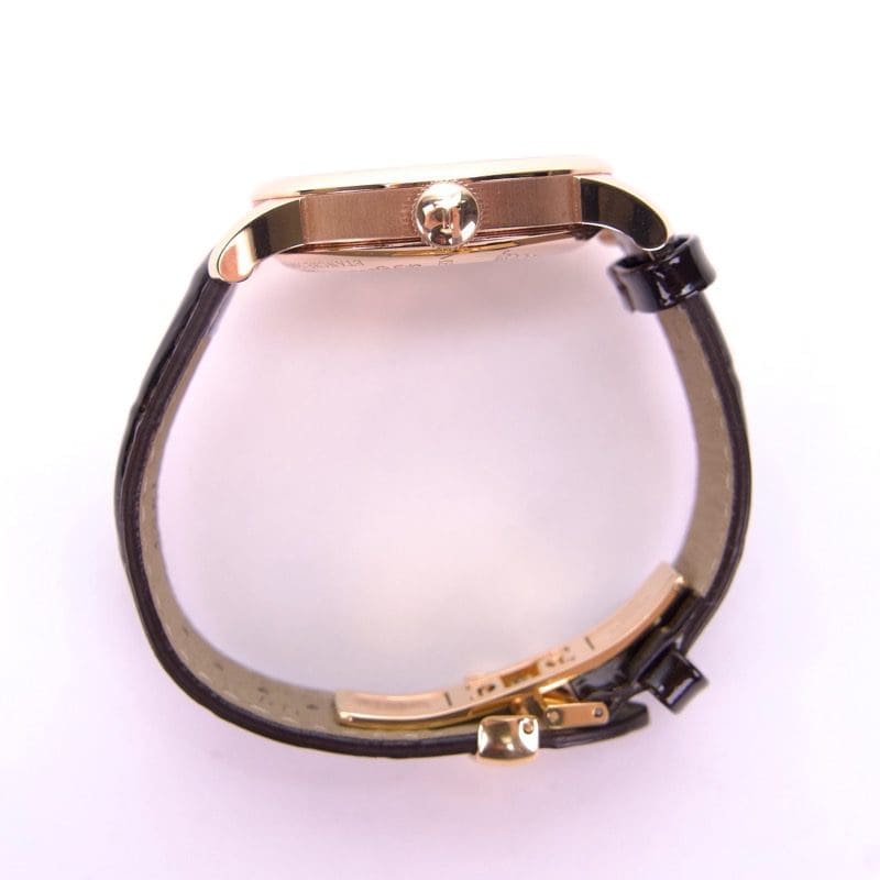 Side view of gold watch with leather strap.