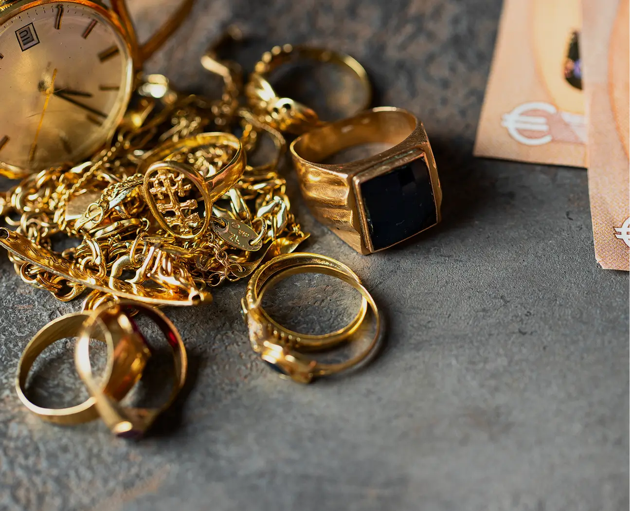 Gold jewelry and watch on textured surface.