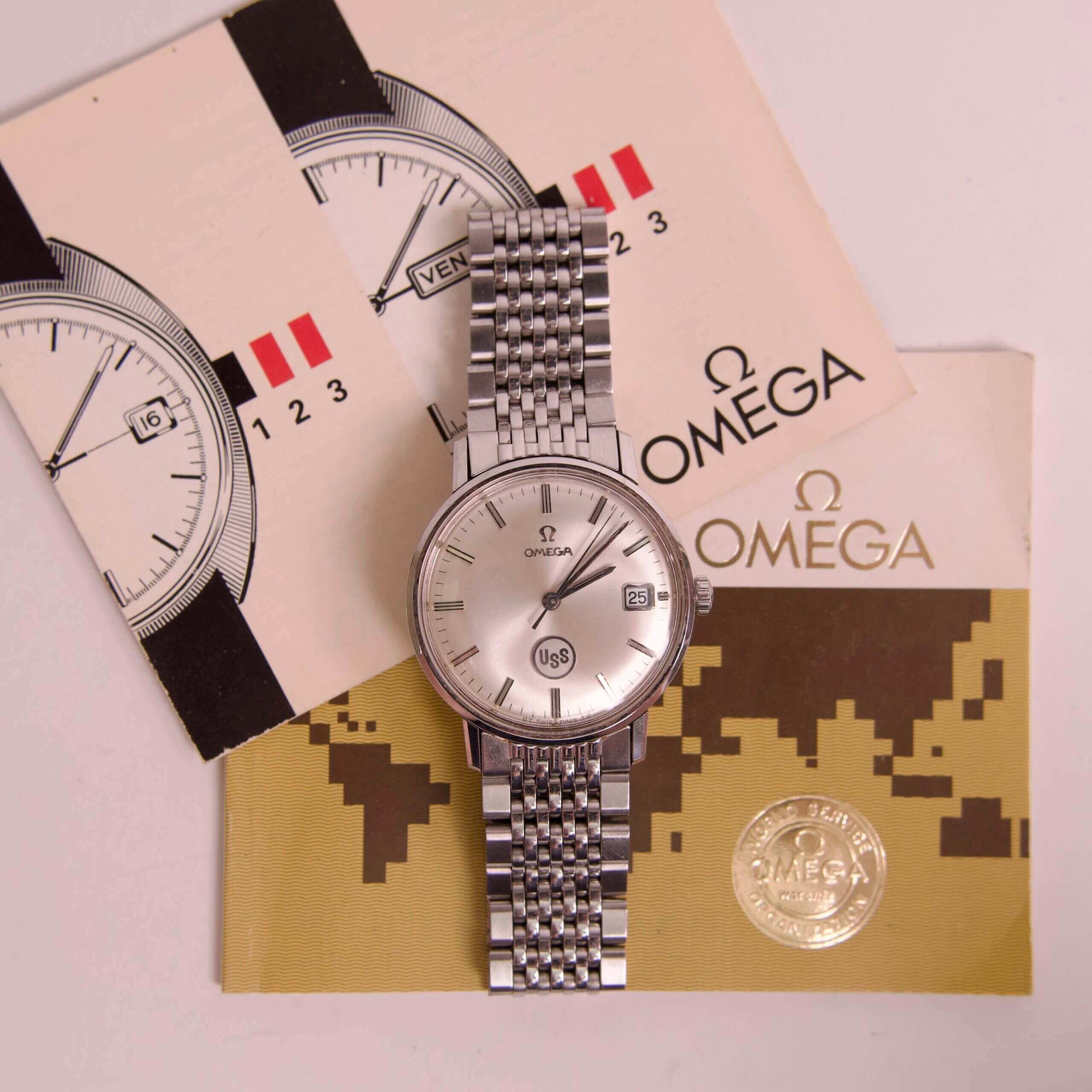 Silver wristwatch with Omega branding and brochures.