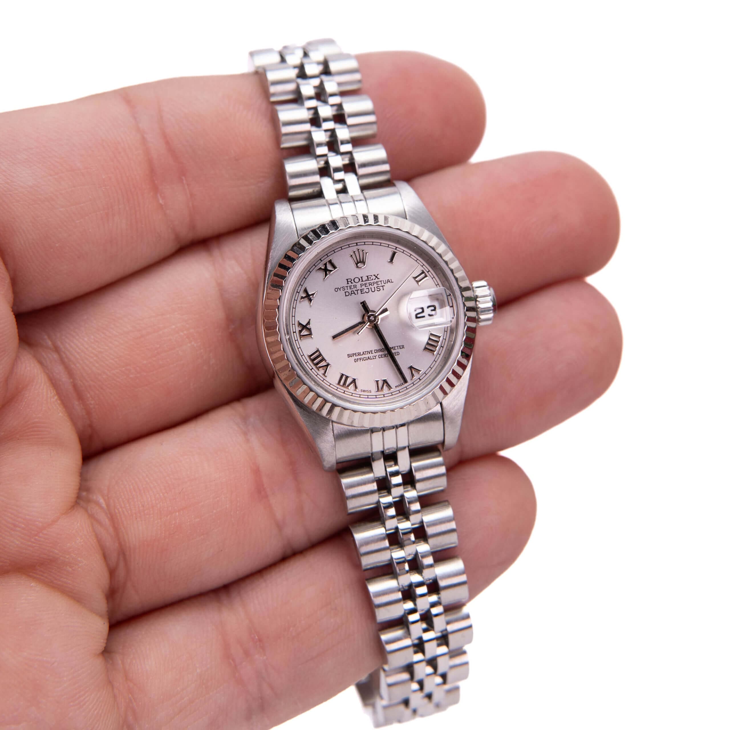 Hand holding a silver wristwatch with date.