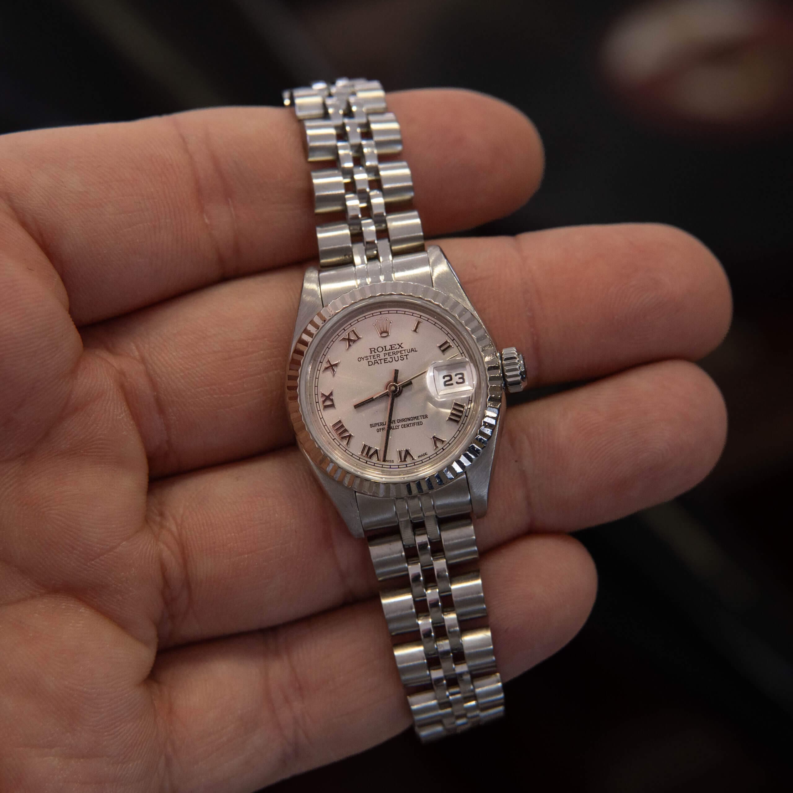 Hand holding a silver wristwatch with date.