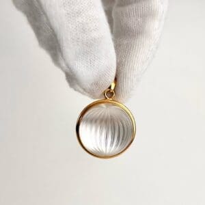 Hand holding gold-framed crystal pendant.
