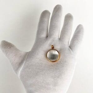 Gold-rimmed pendant in gloved hand.