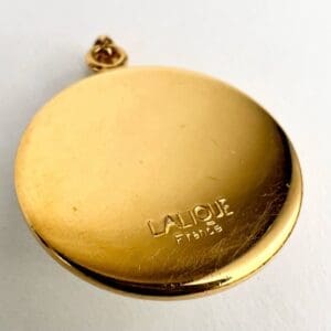 Gold Lalique France medallion on white background.