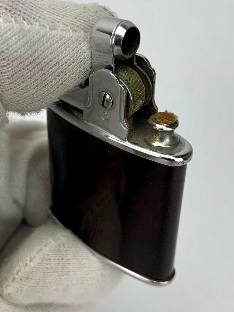 Gloved hand holding vintage metal lighter.